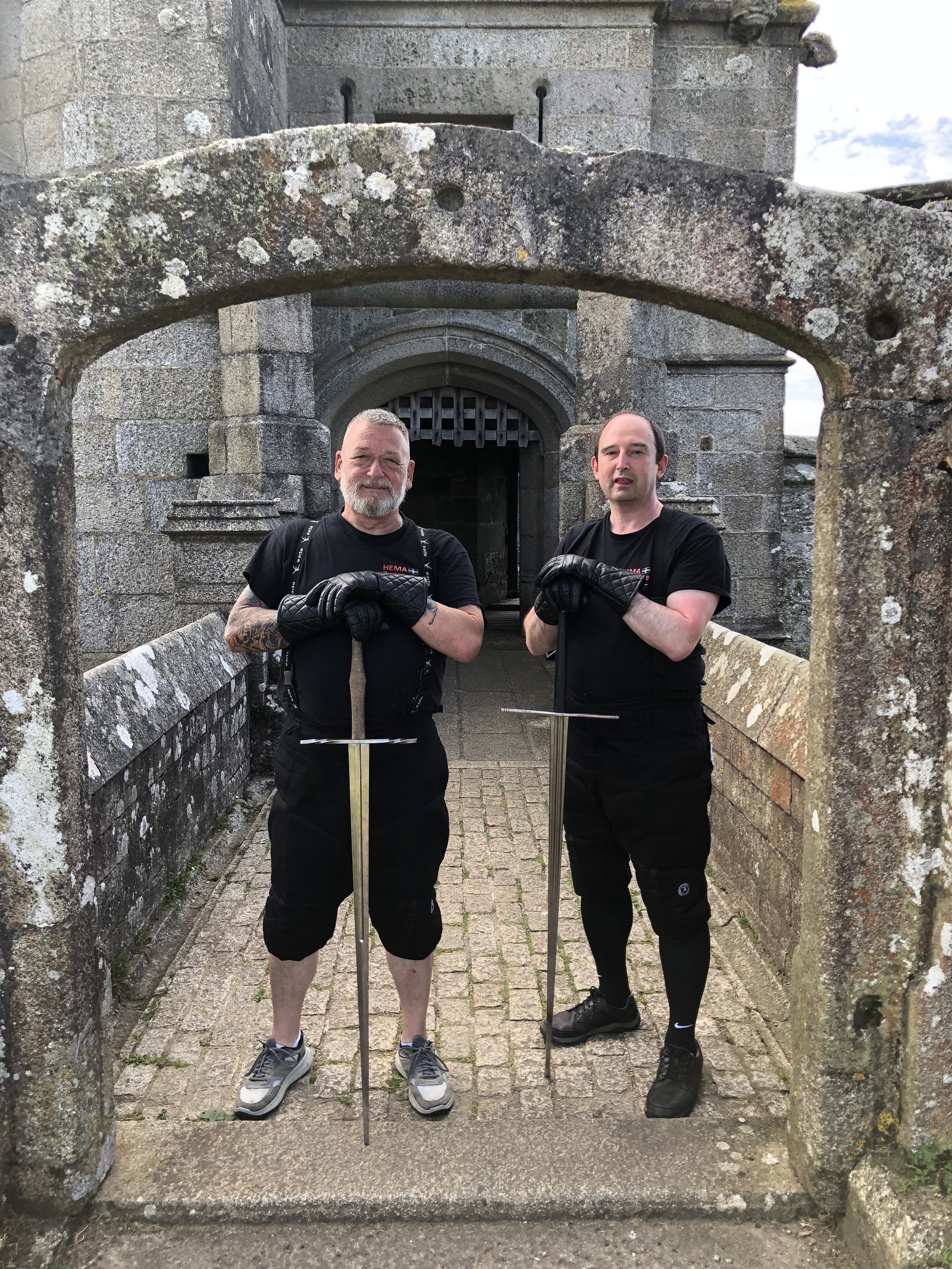Two HEMA Penzance members with longswords on a Pendennis Castle stone bridge